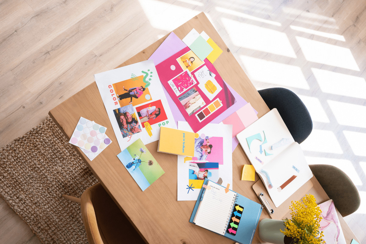 Flat lay of a desk with vibrant colors, diverse photos, color swatches, notebooks, and sticky notes, showcasing playful, strategic branding elements for sustainable marketing planning.