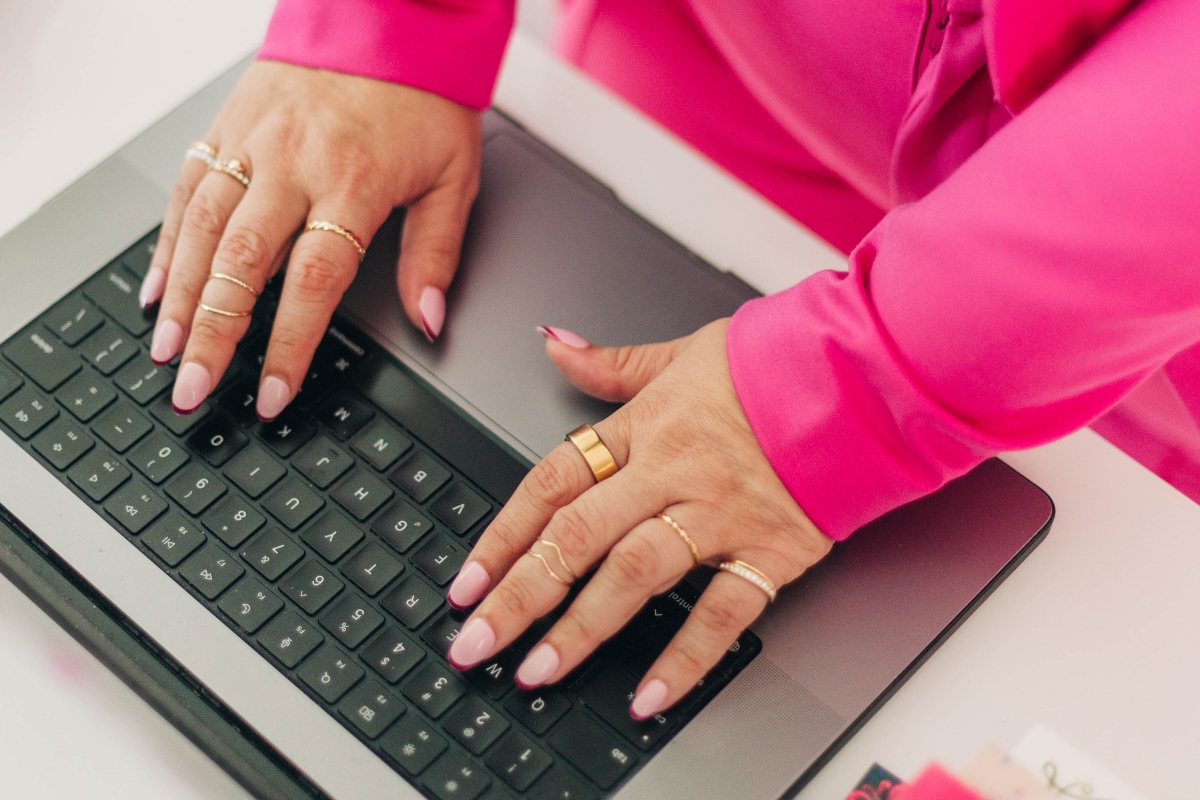 Close-up of a woman in a bold pink outfit typing on a laptop, representing service-based entrepreneurs building affordable small business SEO strategies from home.