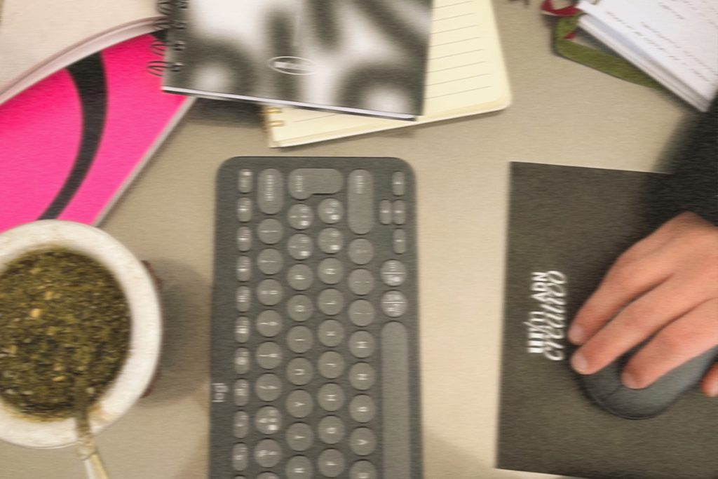 A top down view of a cluttered desk with a keyboard, handwritten notes, tea, and design notebooks in use. The scene suggests the complexity and disorganization that can mirror an outdated website before it is streamlined.