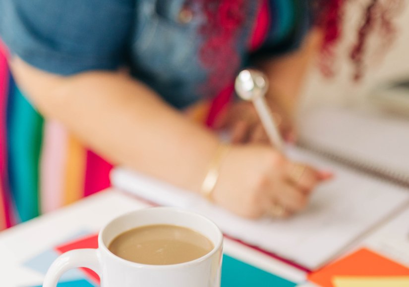 Close up of a desk with a coffee mug that reads "So, it Depends" placed on colorful branding materials labeled "SUNHOUSE SOCIAL" alongside color swatches. In the background, a person writes in a notebook while working through ideas because their website does not reflect their brand.