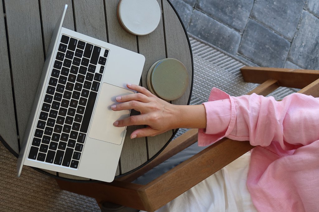 Top down view of a person in a pink shirt using a laptop on an outdoor table with coasters nearby, working on a website that doesn't reflect my brand.