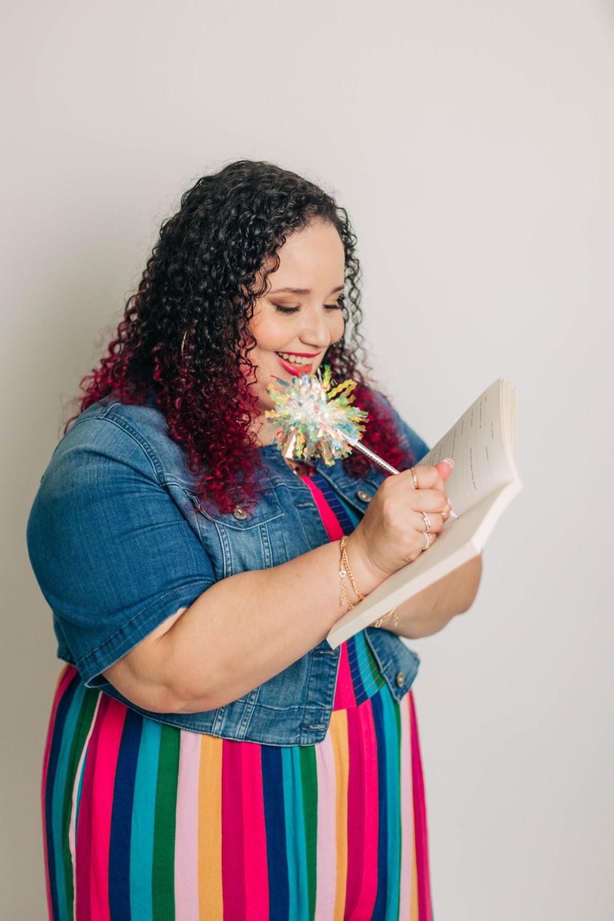 A woman in a colorful striped dress smiles while writing in a notebook with a decorative pen. The focused journaling moment reflects the process of refining website messaging and clarifying ideas.